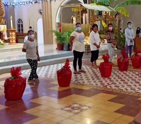 Women in face masks stand spaced apart in a church, red-wrapped baskets lined up on the tiled floor.