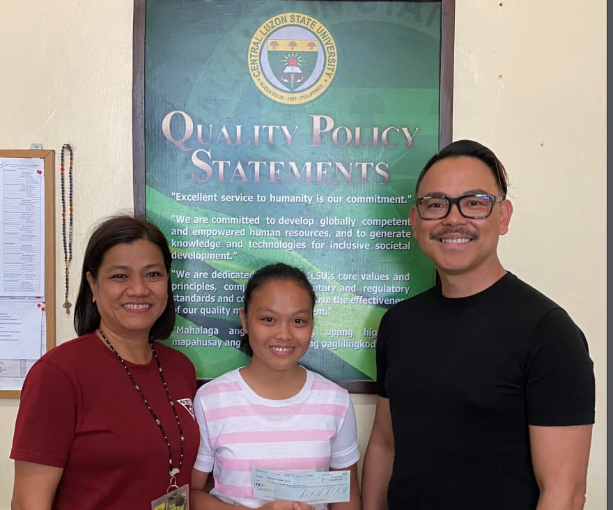 A student holds her scholarship check between her teacher and a MUSA officer at Central Luzon State University.
